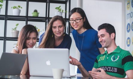 four people watching on white MacBook on top of glass-top table